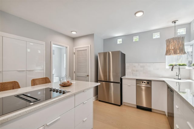 kitchen with sink, hanging light fixtures, stainless steel appliances, light hardwood / wood-style flooring, and white cabinets