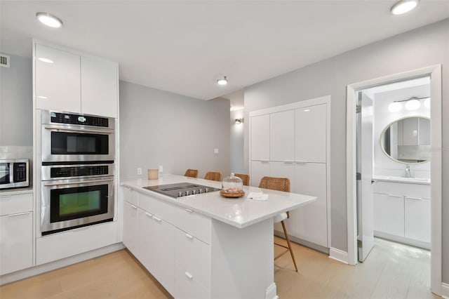 kitchen with a kitchen bar, modern cabinets, white cabinetry, stainless steel appliances, and a peninsula