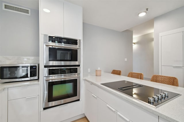 kitchen featuring a kitchen bar, light stone counters, white cabinets, and appliances with stainless steel finishes