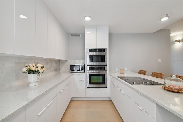 kitchen featuring light stone countertops, light wood-type flooring, tasteful backsplash, stainless steel appliances, and white cabinets