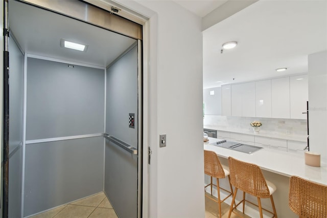 interior space featuring modern cabinets, a kitchen breakfast bar, white cabinetry, elevator, and black electric cooktop