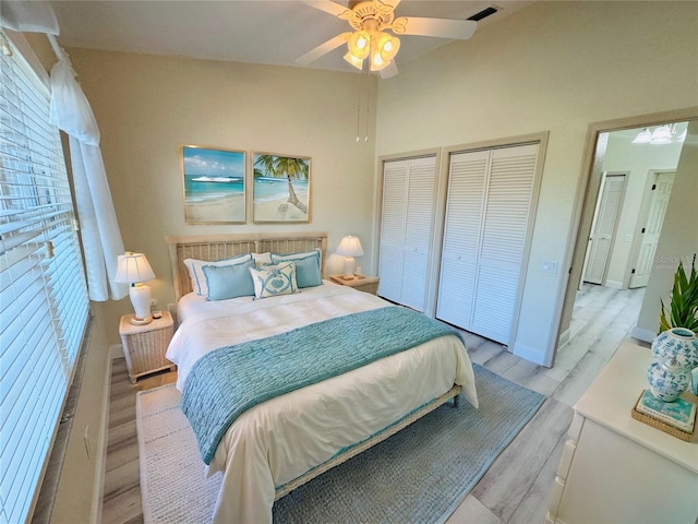 bedroom featuring ceiling fan, light hardwood / wood-style floors, and multiple closets