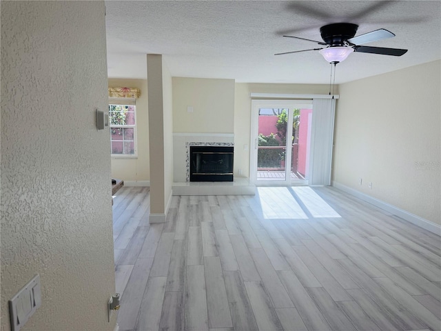 unfurnished living room with a tiled fireplace, ceiling fan, light hardwood / wood-style flooring, and a textured ceiling