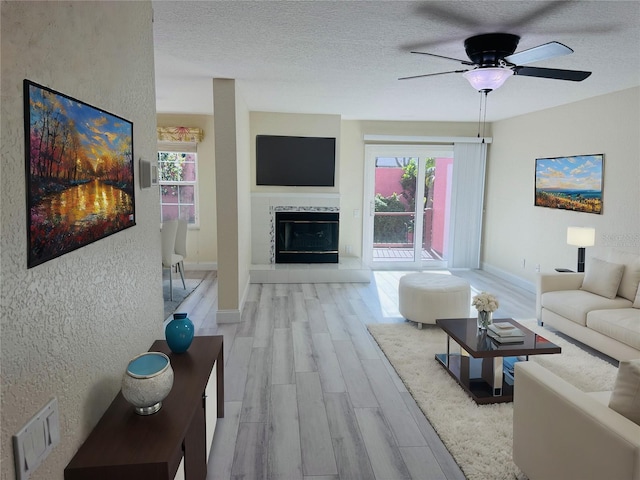 living room featuring a textured ceiling, light wood-type flooring, ceiling fan, and a healthy amount of sunlight