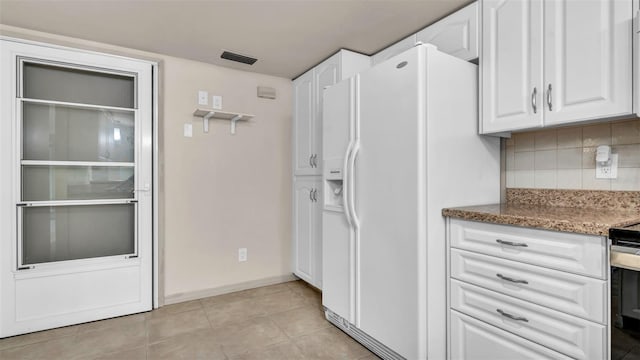 kitchen featuring white fridge with ice dispenser, light tile patterned floors, backsplash, dark stone countertops, and white cabinets