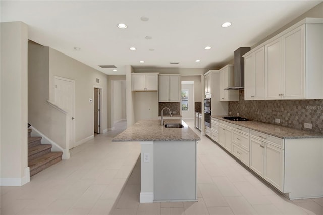 kitchen featuring light stone countertops, gas cooktop, wall chimney exhaust hood, sink, and an island with sink