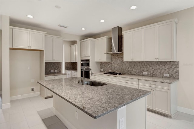 kitchen featuring wall chimney exhaust hood, sink, white cabinetry, and an island with sink