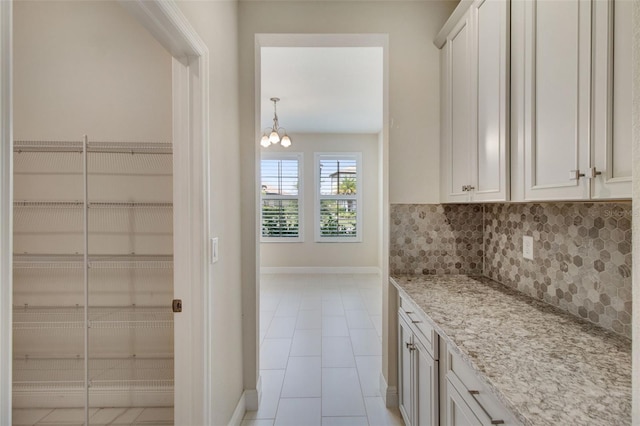 kitchen featuring decorative backsplash, light stone countertops, light tile patterned floors, a notable chandelier, and white cabinetry