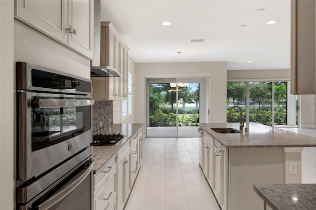 kitchen with appliances with stainless steel finishes, light stone counters, a kitchen island with sink, sink, and decorative light fixtures