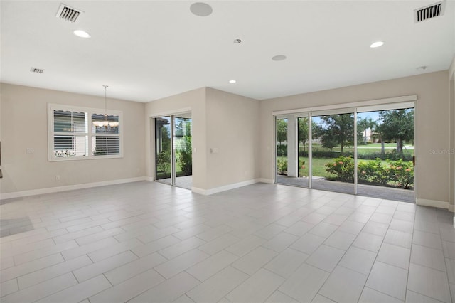 tiled empty room with plenty of natural light and a chandelier