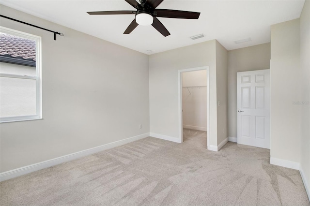 unfurnished bedroom featuring ceiling fan, a closet, a spacious closet, and light carpet