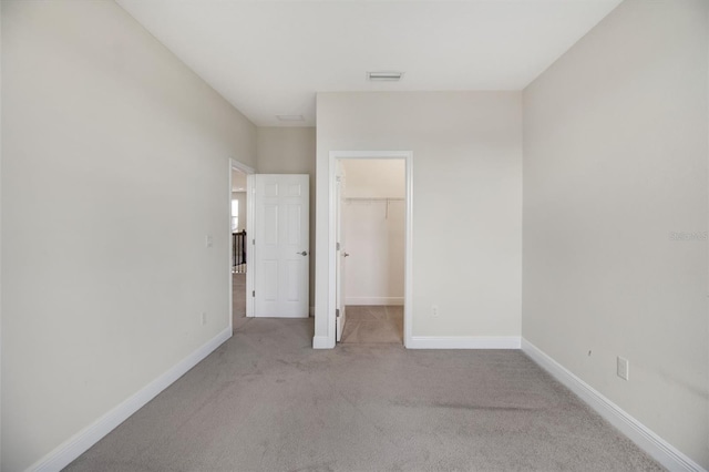 unfurnished bedroom featuring a walk in closet, light colored carpet, and a closet