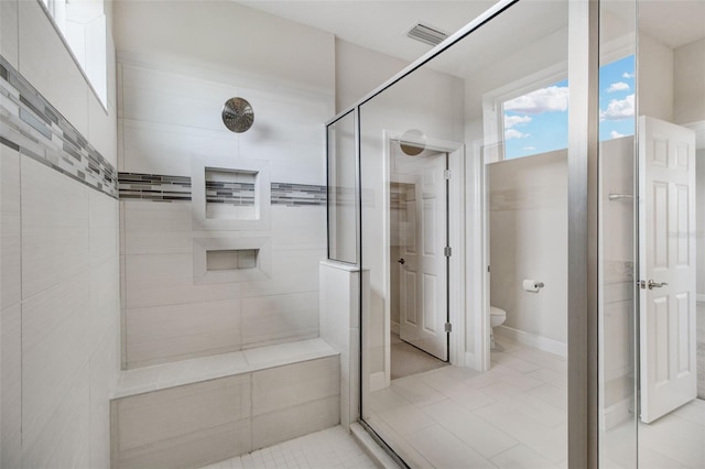 bathroom with tile patterned flooring, toilet, and a tile shower