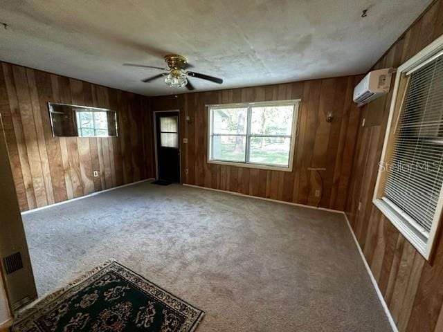 carpeted spare room with wooden walls, ceiling fan, and a wall mounted air conditioner