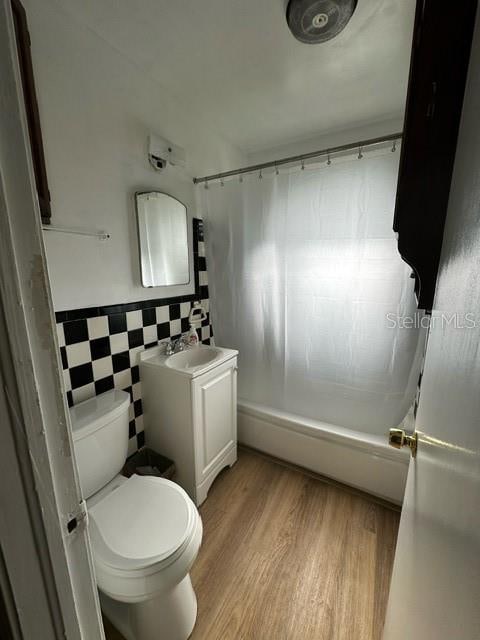 full bathroom featuring toilet, vanity, tile walls, hardwood / wood-style flooring, and shower / bath combination with curtain