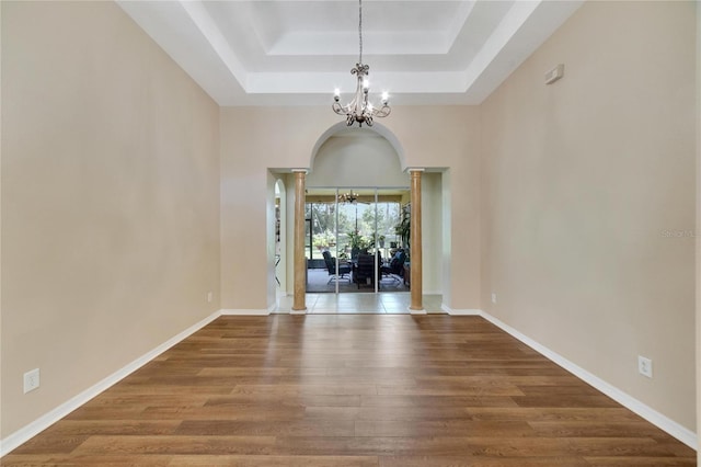 empty room with a tray ceiling, hardwood / wood-style flooring, and a chandelier