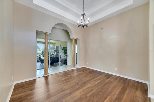 spare room featuring a tray ceiling, wood-type flooring, ornate columns, and a chandelier