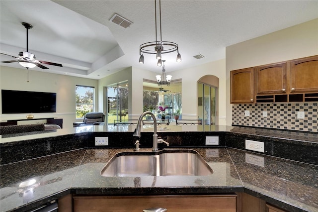 kitchen with ceiling fan with notable chandelier, a tray ceiling, hanging light fixtures, sink, and decorative backsplash