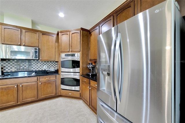 kitchen featuring dark stone countertops, light tile patterned floors, appliances with stainless steel finishes, and decorative backsplash