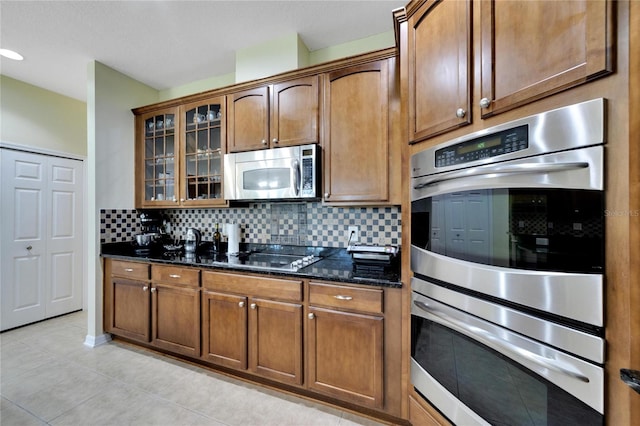 kitchen featuring dark stone countertops, appliances with stainless steel finishes, light tile patterned flooring, and decorative backsplash