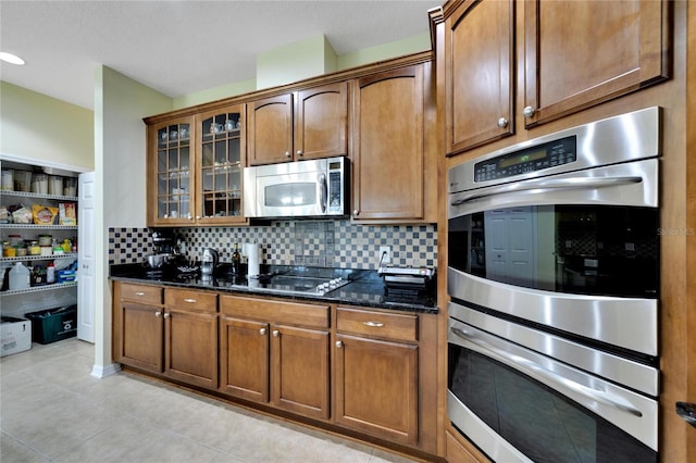 kitchen with dark stone countertops, light tile patterned floors, stainless steel appliances, and backsplash