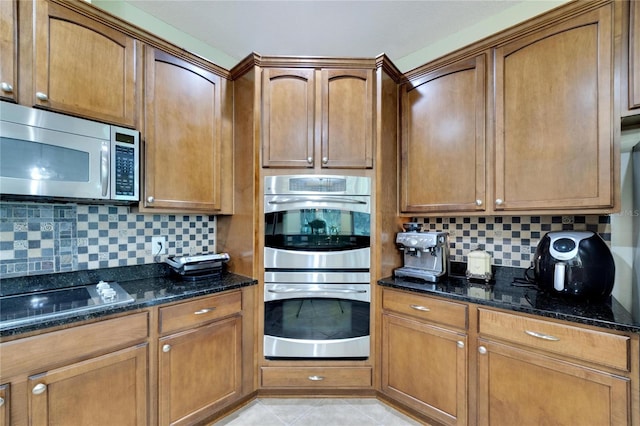 kitchen featuring stainless steel appliances, light tile patterned floors, dark stone counters, and tasteful backsplash