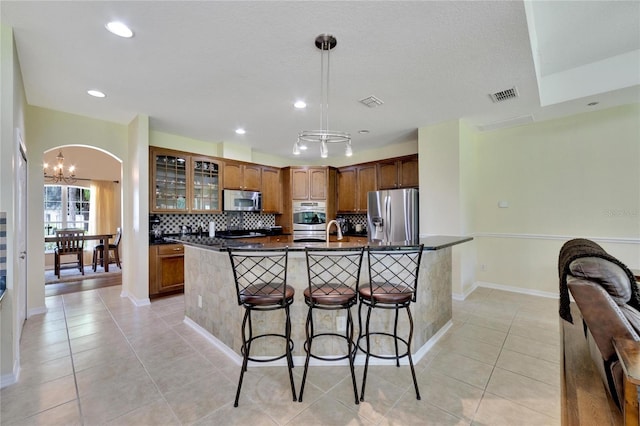 kitchen with a notable chandelier, a kitchen breakfast bar, decorative backsplash, hanging light fixtures, and appliances with stainless steel finishes