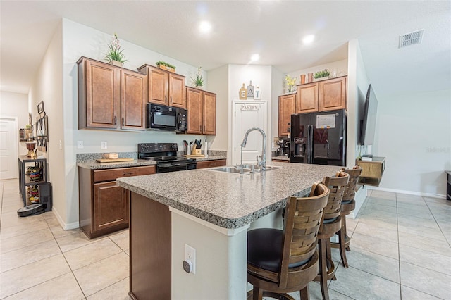 kitchen featuring light tile patterned flooring, a kitchen bar, sink, a kitchen island with sink, and black appliances