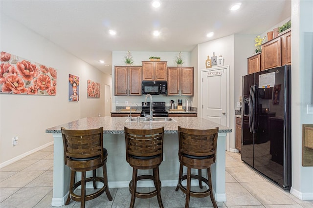 kitchen with a breakfast bar, black appliances, a center island with sink, and light tile patterned flooring