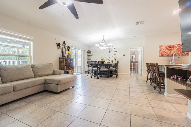 living room featuring sink, lofted ceiling, ceiling fan with notable chandelier, and light tile patterned floors