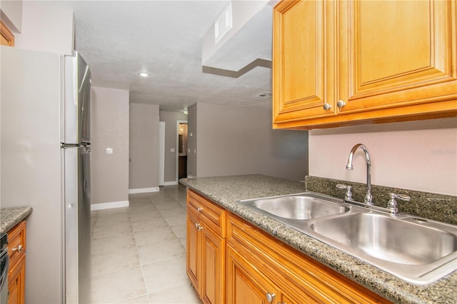 kitchen featuring light tile patterned floors, sink, dark stone counters, and white fridge