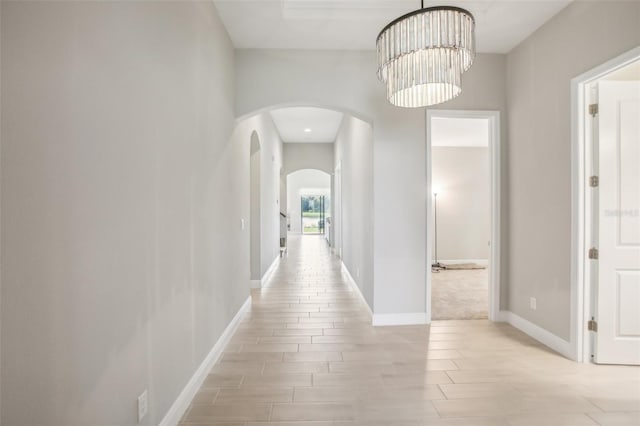 corridor with a chandelier, arched walkways, baseboards, and wood tiled floor