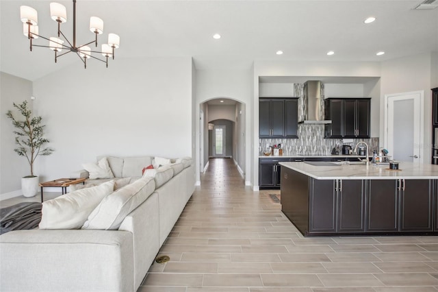 kitchen featuring arched walkways, decorative backsplash, wood tiled floor, open floor plan, and wall chimney exhaust hood