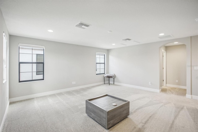 unfurnished room with visible vents, arched walkways, baseboards, and light colored carpet