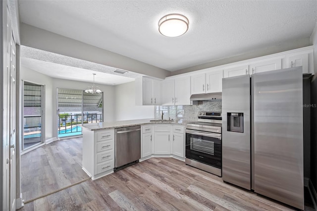 kitchen with light wood finished floors, white cabinets, under cabinet range hood, appliances with stainless steel finishes, and a chandelier