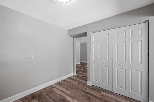 unfurnished bedroom with dark wood-style floors, a textured ceiling, a closet, and baseboards