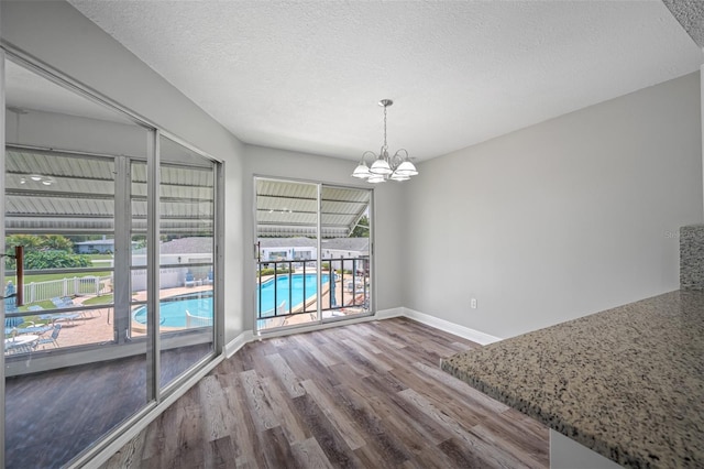 unfurnished dining area with a textured ceiling, wood finished floors, baseboards, and a chandelier