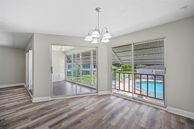 unfurnished dining area featuring baseboards, a notable chandelier, wood finished floors, and a textured ceiling