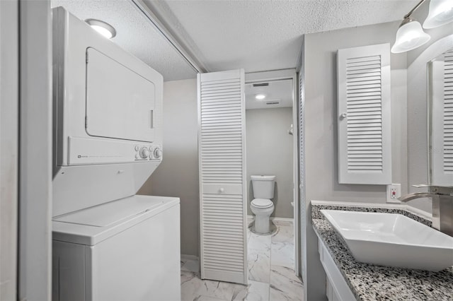 laundry area with stacked washer / dryer, baseboards, marble finish floor, a textured ceiling, and a sink