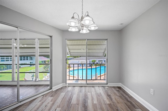 empty room featuring a textured ceiling, wood finished floors, baseboards, and a chandelier