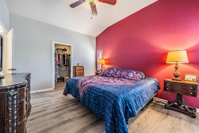 bedroom featuring a walk in closet, a closet, hardwood / wood-style flooring, lofted ceiling, and ceiling fan