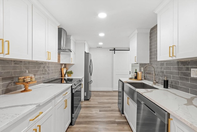 kitchen featuring backsplash, appliances with stainless steel finishes, white cabinetry, light wood-type flooring, and wall chimney range hood