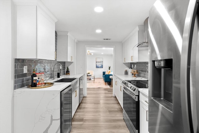 kitchen with wall chimney exhaust hood, decorative backsplash, light hardwood / wood-style flooring, and appliances with stainless steel finishes