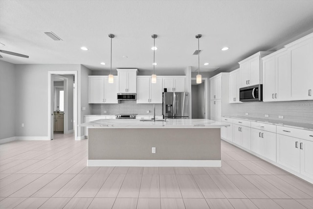 kitchen featuring pendant lighting, white cabinets, stainless steel appliances, and a kitchen island with sink