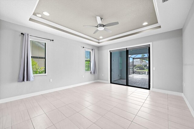 tiled empty room with ceiling fan and a tray ceiling