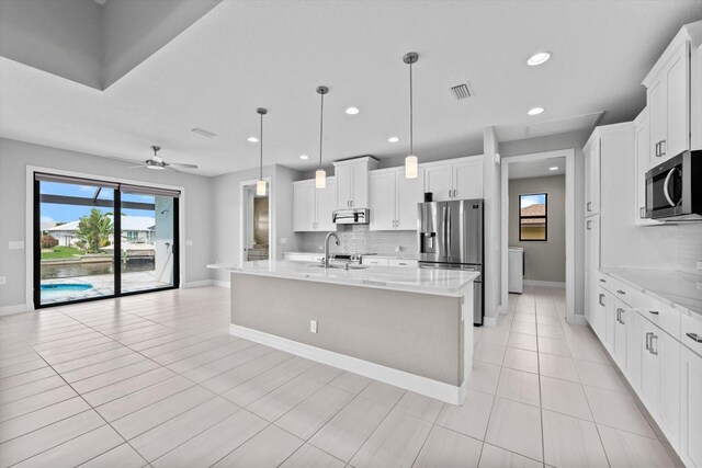 kitchen featuring white cabinets, appliances with stainless steel finishes, a center island with sink, and decorative light fixtures