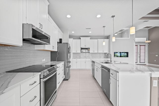 kitchen with white cabinetry, sink, stainless steel appliances, decorative light fixtures, and a center island with sink