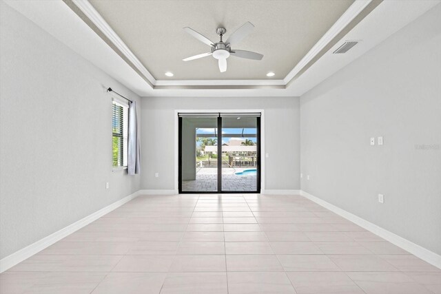 tiled empty room featuring ceiling fan, a raised ceiling, and ornamental molding