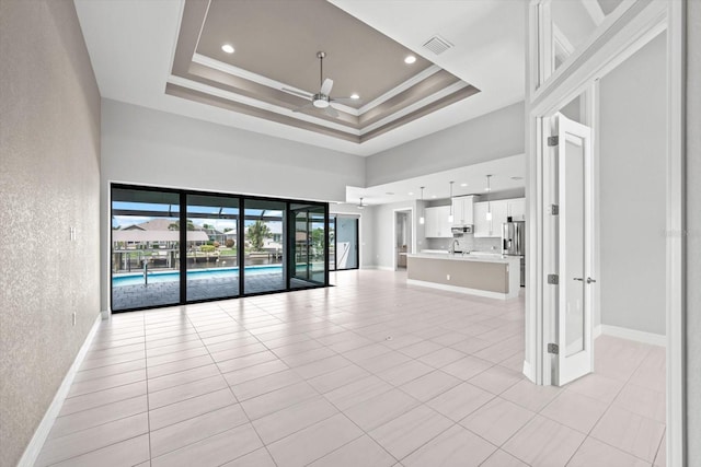 unfurnished living room featuring ceiling fan, light tile patterned floors, a high ceiling, and a tray ceiling