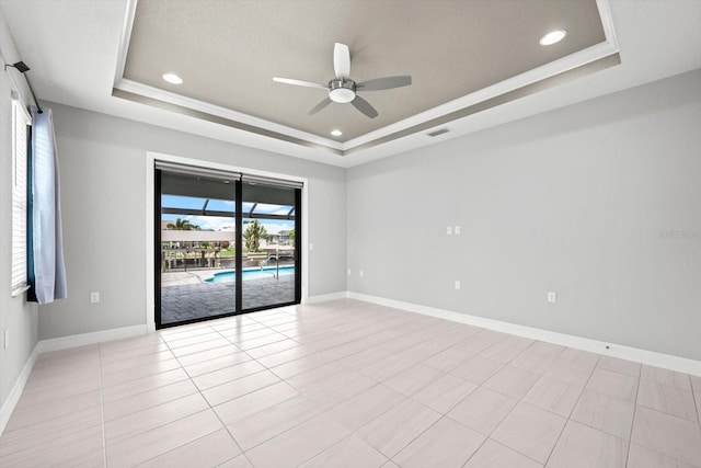 empty room with ceiling fan, light tile patterned flooring, ornamental molding, and a tray ceiling